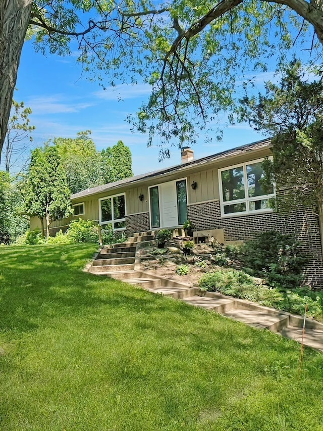 ranch-style home featuring brick siding, a chimney, a front yard, and board and batten siding