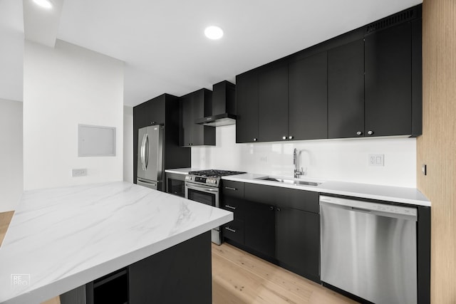 kitchen with wall chimney range hood, sink, appliances with stainless steel finishes, light hardwood / wood-style floors, and kitchen peninsula