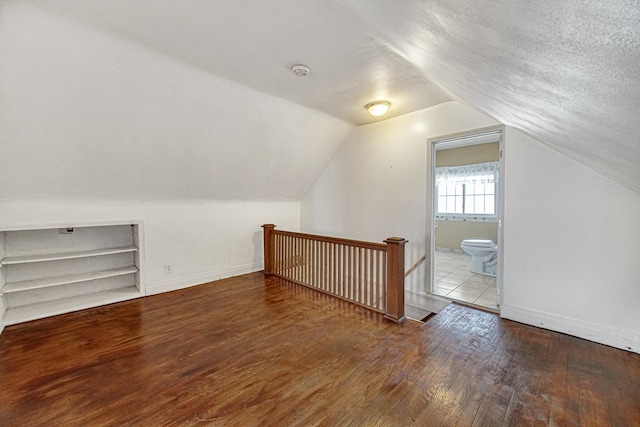 additional living space with lofted ceiling, wood-type flooring, and a textured ceiling