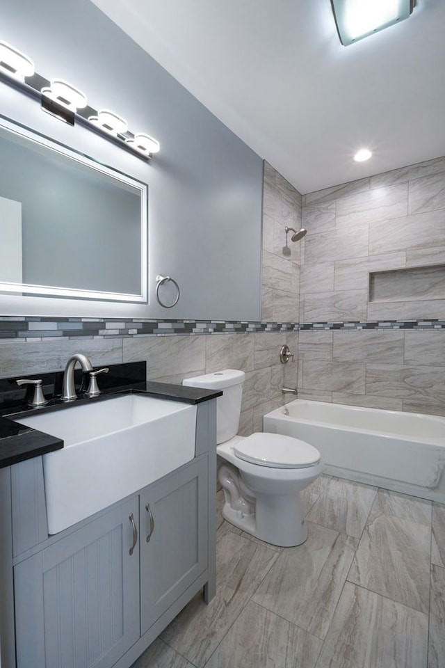 full bathroom featuring vanity, toilet, tiled shower / bath, and tile walls