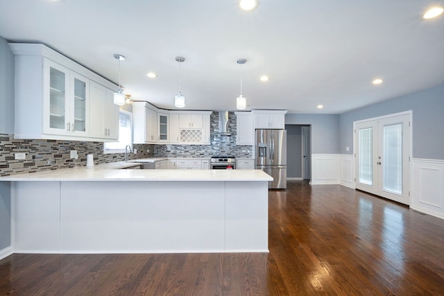 kitchen with white cabinets, wall chimney range hood, appliances with stainless steel finishes, decorative light fixtures, and kitchen peninsula