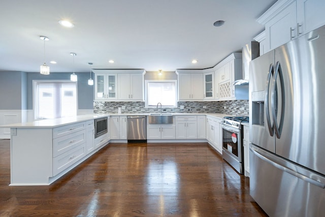 kitchen with stainless steel appliances, sink, wall chimney range hood, decorative light fixtures, and white cabinets