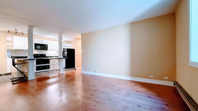 kitchen featuring black appliances, light wood-type flooring, a breakfast bar, a baseboard heating unit, and white cabinets