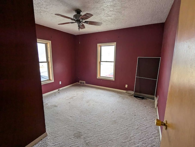 empty room with ceiling fan, light colored carpet, a healthy amount of sunlight, and a textured ceiling