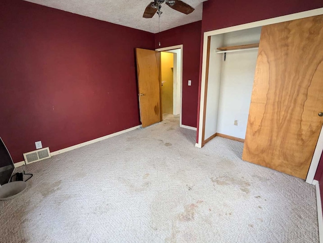 unfurnished bedroom featuring ceiling fan, light colored carpet, a textured ceiling, and a closet