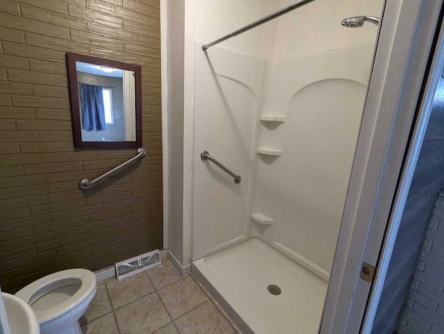 bathroom with toilet, tile patterned flooring, brick wall, and walk in shower