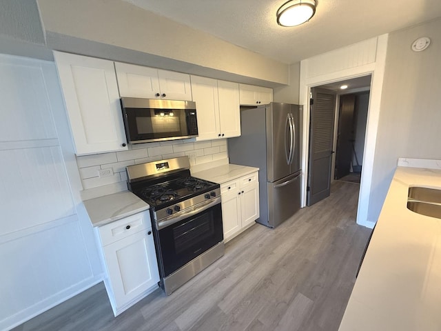 kitchen featuring tasteful backsplash, white cabinetry, light hardwood / wood-style flooring, and appliances with stainless steel finishes