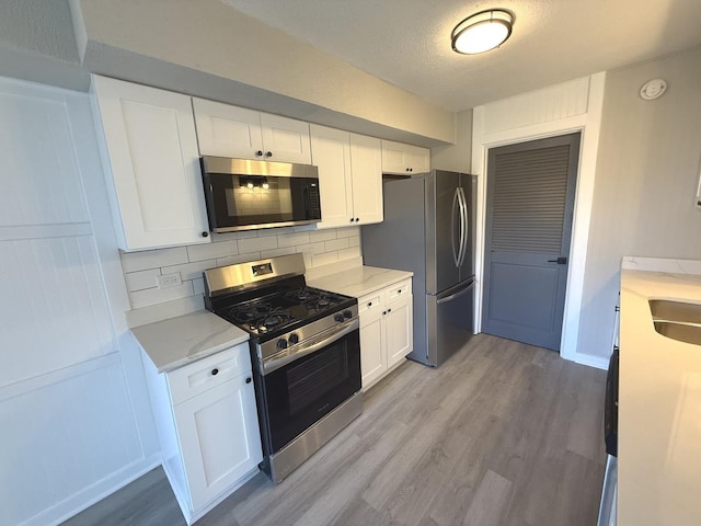 kitchen with white cabinets, decorative backsplash, light wood-type flooring, and stainless steel appliances