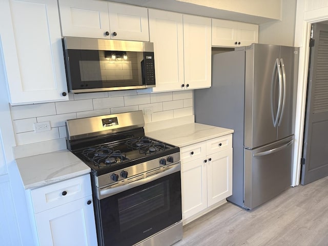 kitchen featuring white cabinets, light wood-type flooring, appliances with stainless steel finishes, tasteful backsplash, and light stone counters