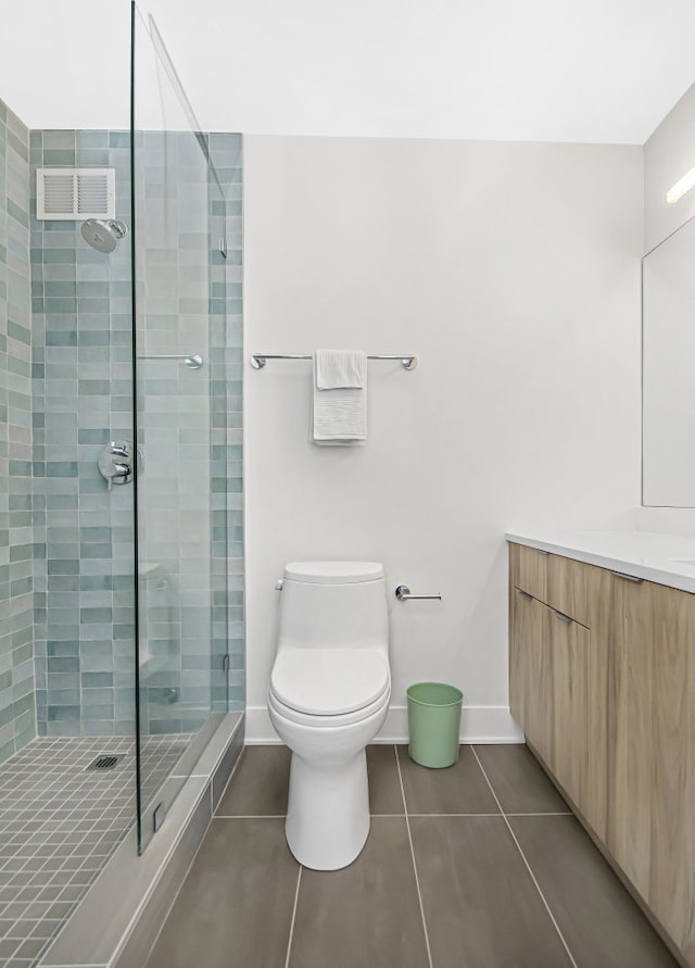 bathroom featuring vanity, tile patterned flooring, toilet, and a tile shower