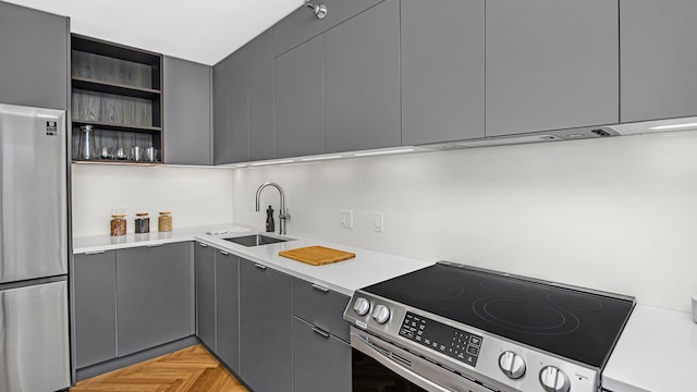 kitchen with gray cabinetry, sink, light parquet flooring, and appliances with stainless steel finishes