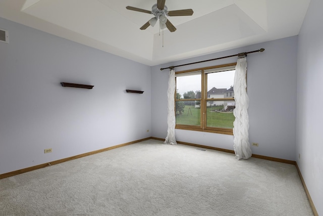 empty room featuring ceiling fan, a raised ceiling, and light colored carpet