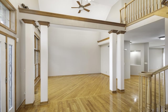 unfurnished living room featuring decorative columns, ceiling fan, a towering ceiling, and hardwood / wood-style flooring