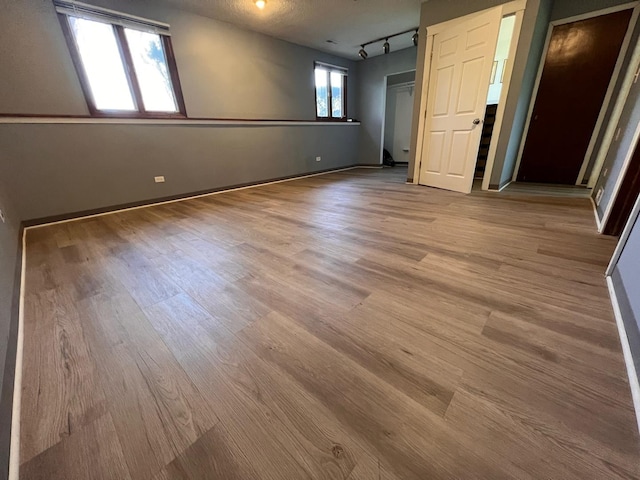 unfurnished bedroom featuring multiple windows, rail lighting, light hardwood / wood-style floors, and a textured ceiling