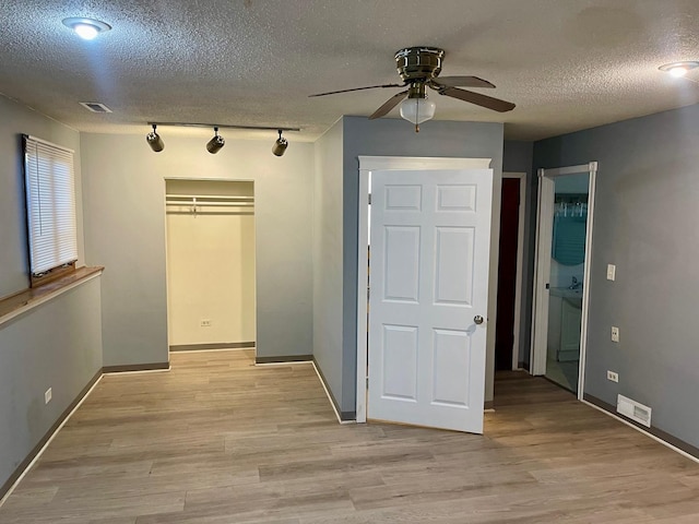 unfurnished bedroom with ceiling fan, rail lighting, light hardwood / wood-style floors, and a textured ceiling