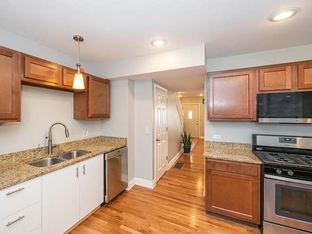 kitchen with sink, light stone counters, hanging light fixtures, light hardwood / wood-style flooring, and stainless steel appliances