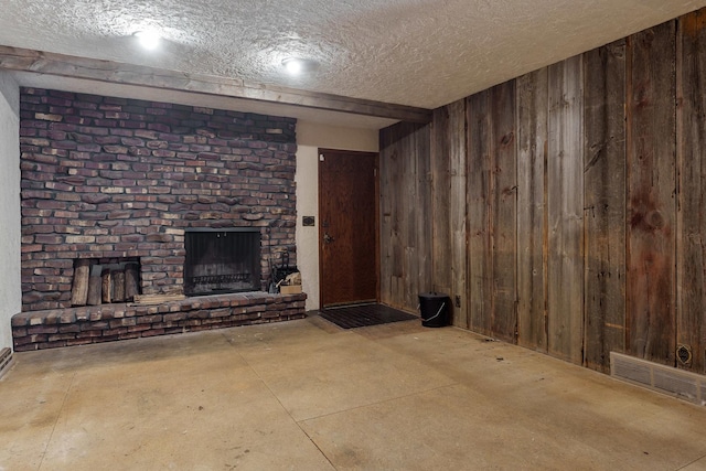 basement featuring wooden walls, a textured ceiling, and a brick fireplace