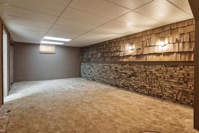 basement with carpet flooring, a paneled ceiling, and brick wall