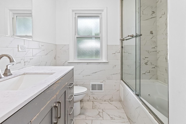 full bathroom featuring vanity, toilet, a wealth of natural light, and bath / shower combo with glass door