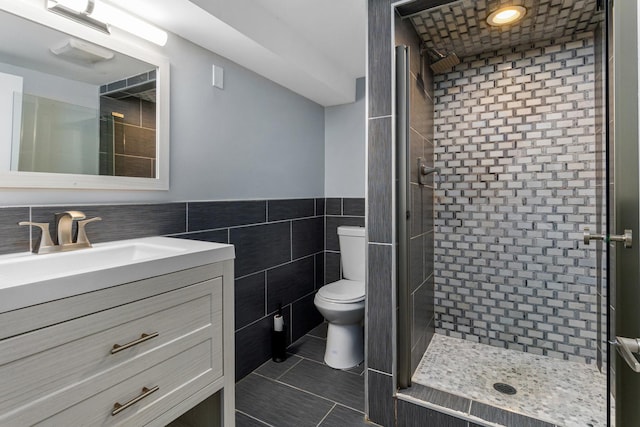 bathroom with tile patterned floors, a tile shower, vanity, tile walls, and toilet