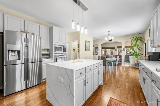 kitchen with hanging light fixtures, light stone countertops, a kitchen island, white cabinetry, and stainless steel appliances