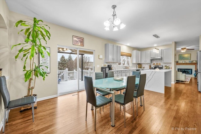 dining space with ceiling fan with notable chandelier and light hardwood / wood-style floors