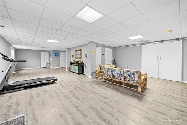 workout room with a paneled ceiling and light wood-type flooring