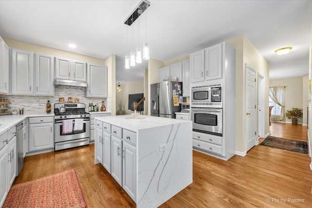 kitchen with white cabinets, appliances with stainless steel finishes, decorative light fixtures, and a kitchen island