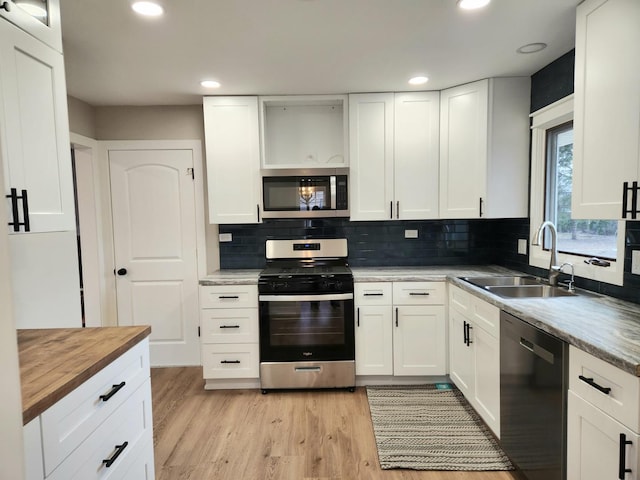 kitchen with sink, appliances with stainless steel finishes, tasteful backsplash, white cabinets, and light wood-type flooring