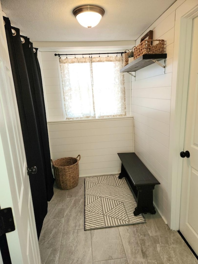 mudroom with wooden walls and a textured ceiling