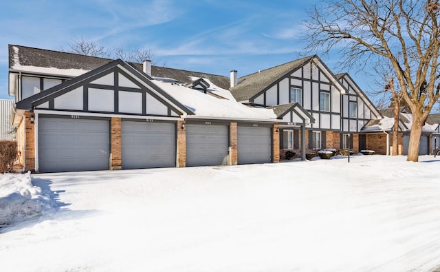 tudor home with a garage, brick siding, a chimney, and stucco siding