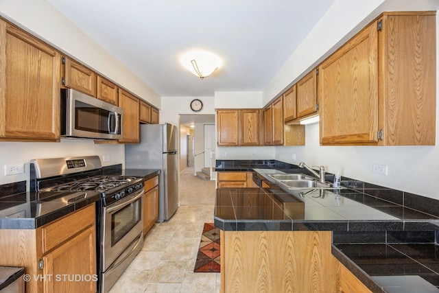 kitchen with stainless steel appliances, brown cabinetry, a sink, and tile countertops