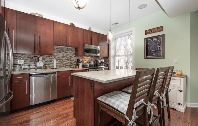 kitchen with appliances with stainless steel finishes, dark wood-type flooring, sink, decorative light fixtures, and a kitchen island