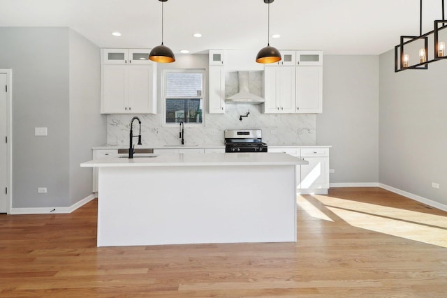 kitchen with gas range, an island with sink, white cabinetry, and wall chimney range hood