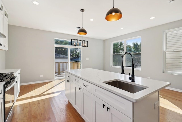 kitchen featuring light stone counters, sink, pendant lighting, white cabinets, and stainless steel gas stove