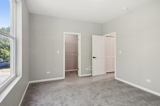 unfurnished bedroom featuring a closet, a spacious closet, light carpet, and multiple windows