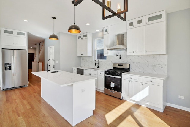 kitchen featuring appliances with stainless steel finishes, wall chimney exhaust hood, sink, a center island with sink, and white cabinetry