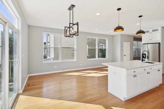 kitchen with stainless steel refrigerator with ice dispenser, light hardwood / wood-style flooring, white cabinetry, hanging light fixtures, and an island with sink