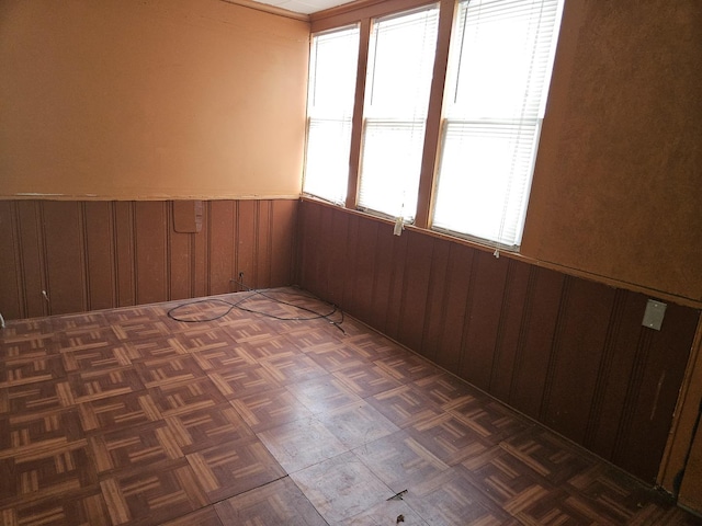 unfurnished room with plenty of natural light, wood walls, and dark parquet floors