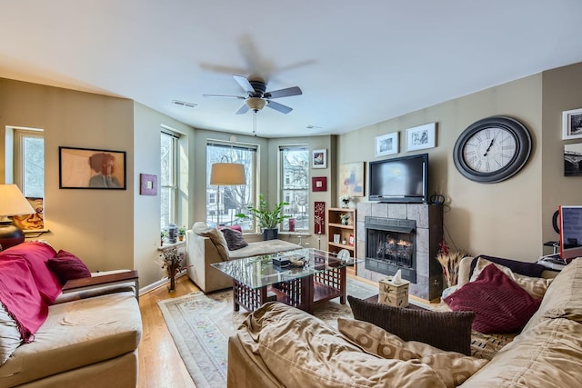 living room featuring light wood-type flooring, a tiled fireplace, and ceiling fan