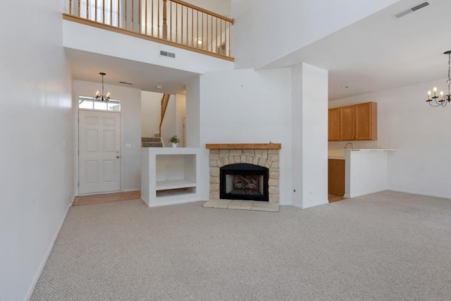 unfurnished living room featuring a high ceiling, light colored carpet, a notable chandelier, and a stone fireplace