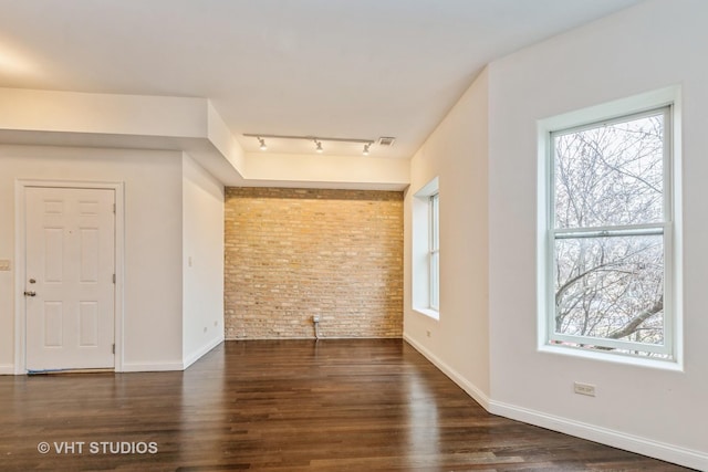 spare room featuring rail lighting, brick wall, and dark hardwood / wood-style floors