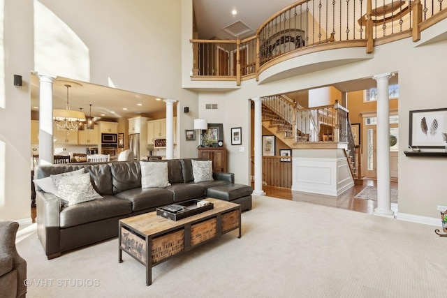 living room featuring decorative columns, light colored carpet, stairway, a high ceiling, and a chandelier