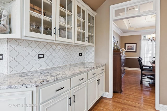 kitchen featuring a tray ceiling, light wood finished floors, glass insert cabinets, white cabinets, and light stone countertops