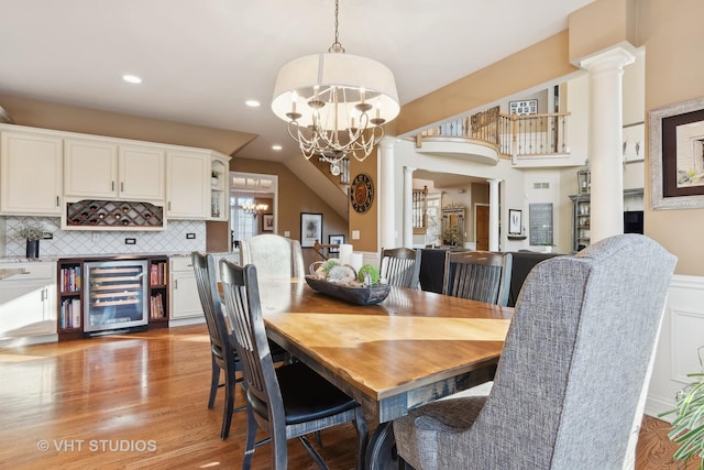 dining space featuring beverage cooler, light wood-style flooring, an inviting chandelier, ornate columns, and recessed lighting