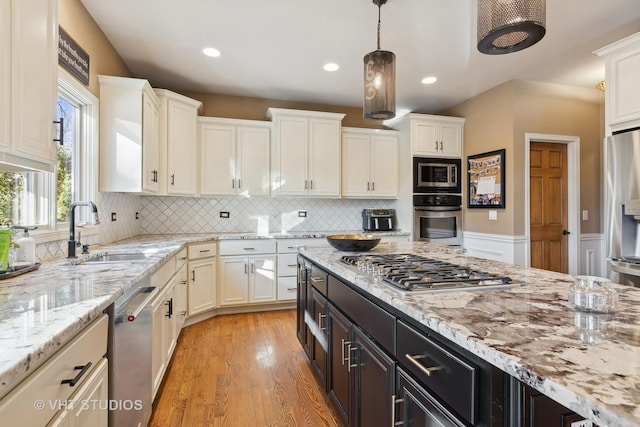 kitchen featuring stainless steel appliances, white cabinets, a sink, and hanging light fixtures