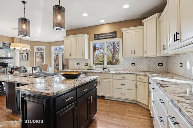 kitchen featuring light wood-style flooring, light stone countertops, hanging light fixtures, dark cabinetry, and decorative backsplash