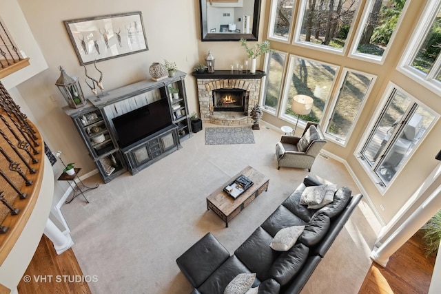 living area featuring a stone fireplace, plenty of natural light, a high ceiling, and baseboards