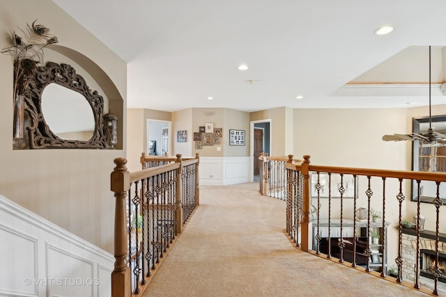 corridor featuring light carpet, recessed lighting, a decorative wall, and an upstairs landing