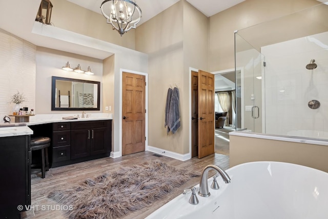 bathroom with a freestanding tub, a notable chandelier, wood finished floors, vanity, and a shower stall